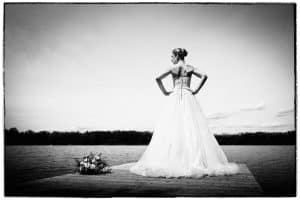 Braut steht auf einem Steg am See.